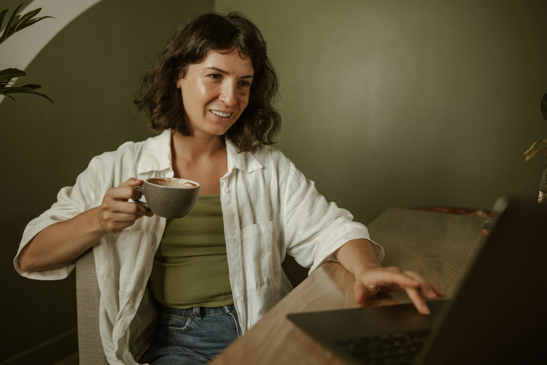 a woman sitting at a table with a laptop and a cup of coffee